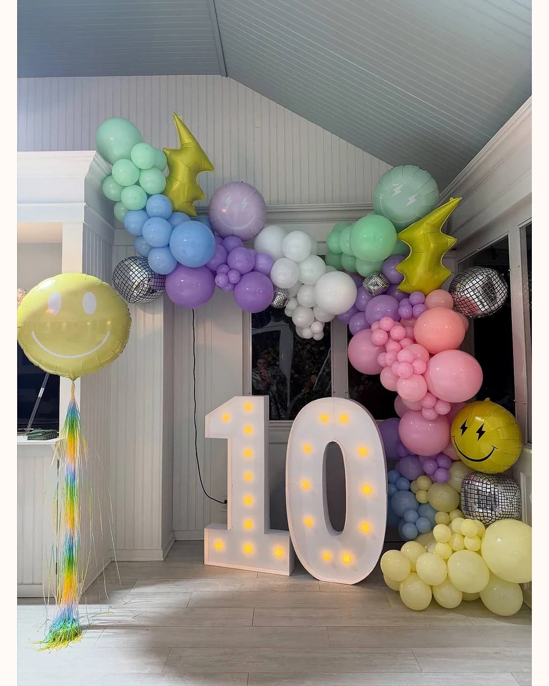 Pastel balloon installation with marquee ten numbers and smiley accents for a birthday party