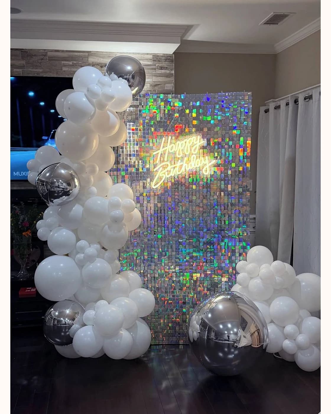 White birthday setup with shimmer wall, white balloons, and a happy birthday neon sign