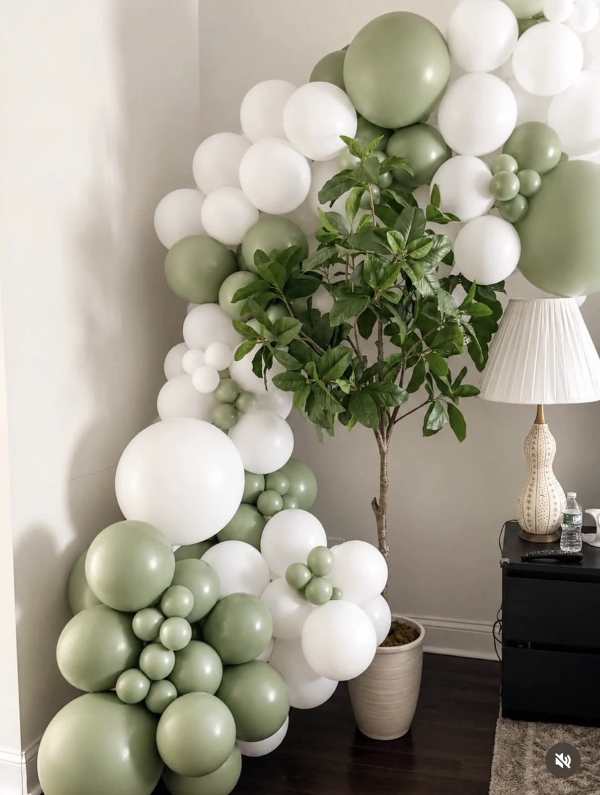 Sage green and white organic balloon garland arranged around an indoor tree